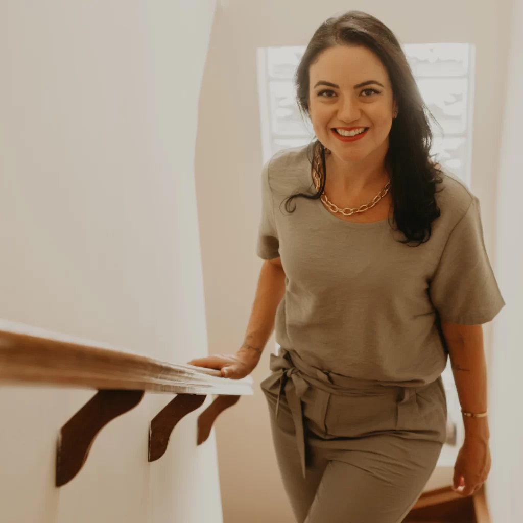 Mariana Drago subindo uma escada, olhando para a câmera com um sorriso